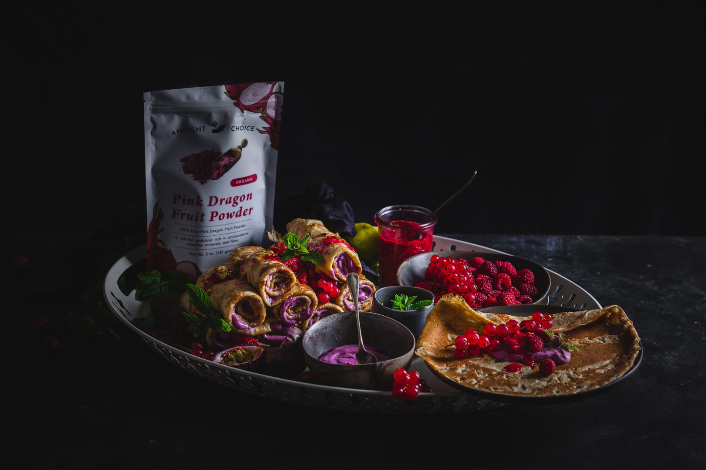 Dragon fruit crepes made with Ancient Choice pink dragon fruit powder, served with berries, pink cream, and raspberry sauce on a silver tray.