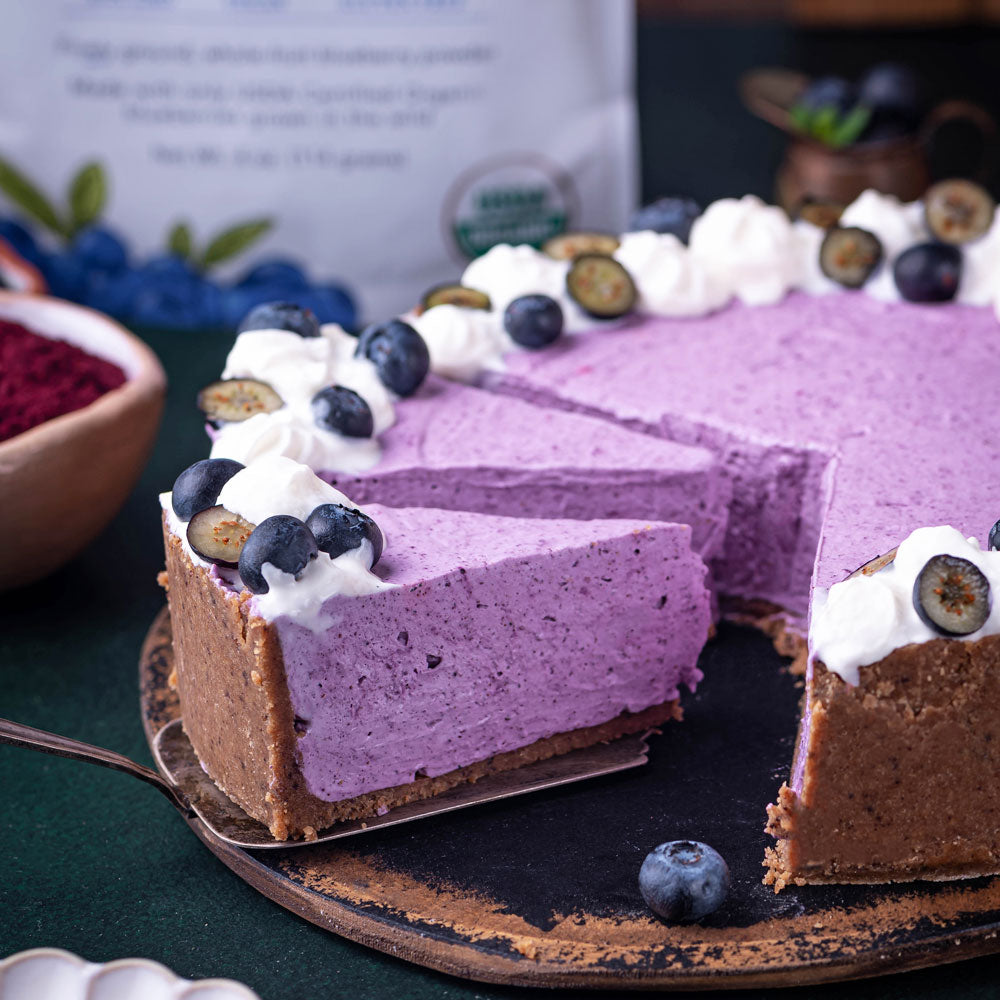 Cheesecake made with wild blueberry powder, topped with cream and berries on rustic plate