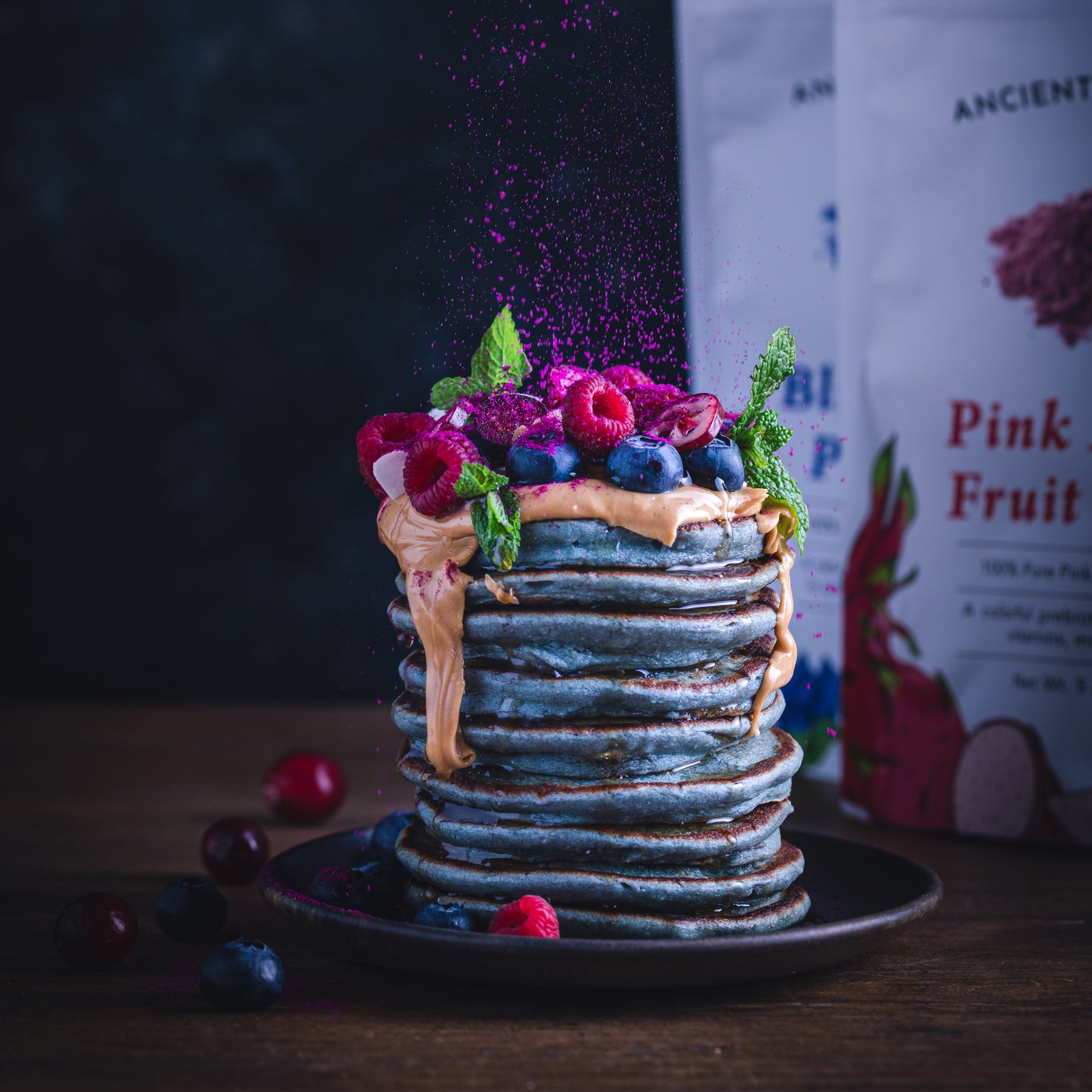 Stack of butterfly pea flower pancakes topped with peanut butter, fresh berries, and a sprinkle of dragon fruit powder.