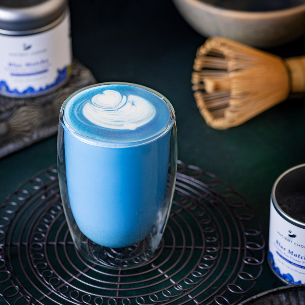 Ancient Choice Blue Matcha Latte served in a clear glass with heart-shaped foam art