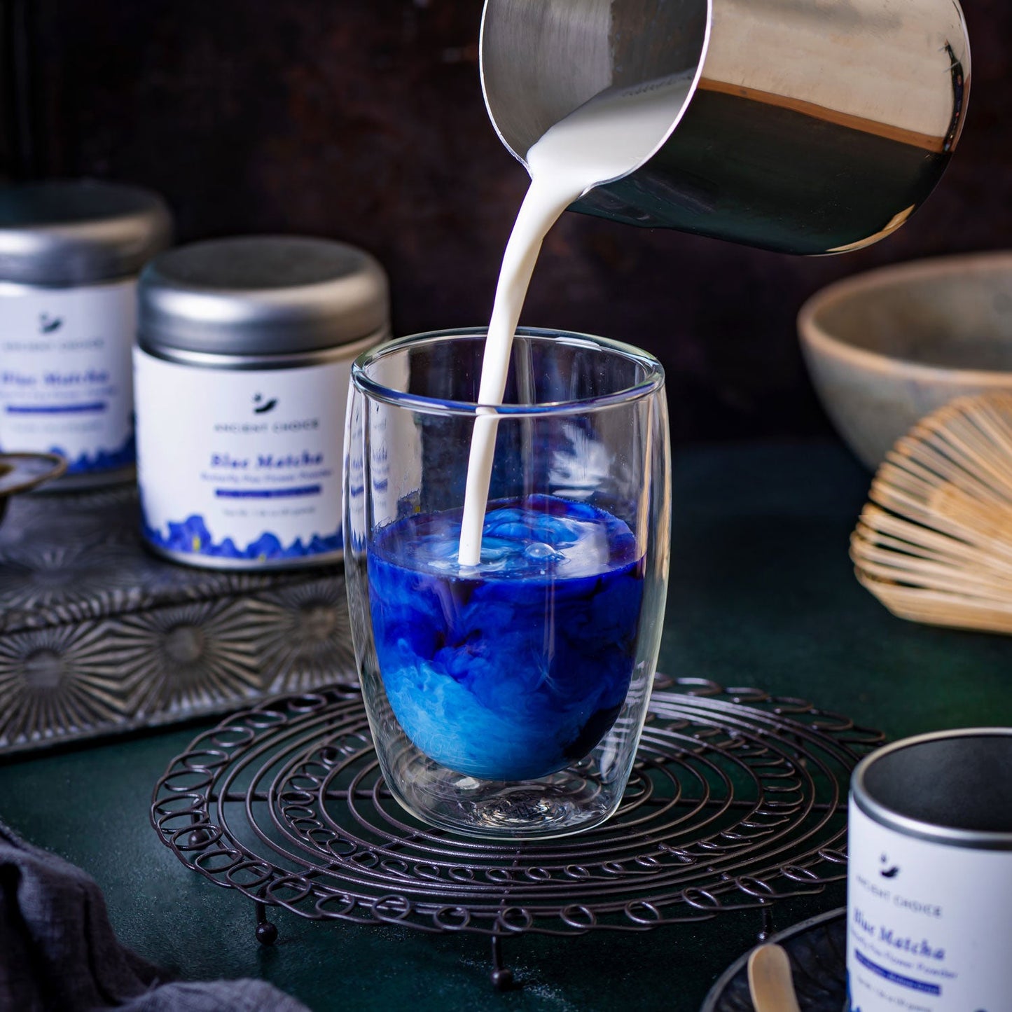 Steamed milk being poured into a glass of blue matcha tea