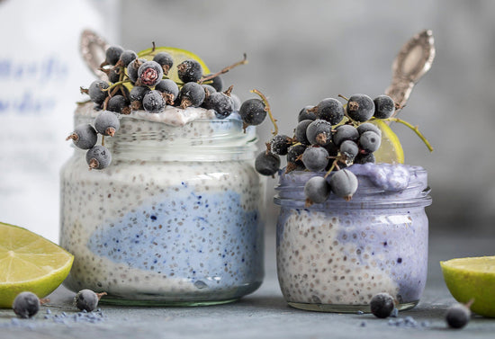 Two glass jars filled with chia pudding and blue butterfly pea powder, garnished with blueberries and a slice of lime