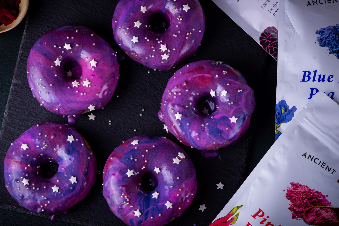 Galaxy donuts with colorful glaze made using Ancient Choice antioxidant powders as natural food coloring, topped with white star sprinkles.