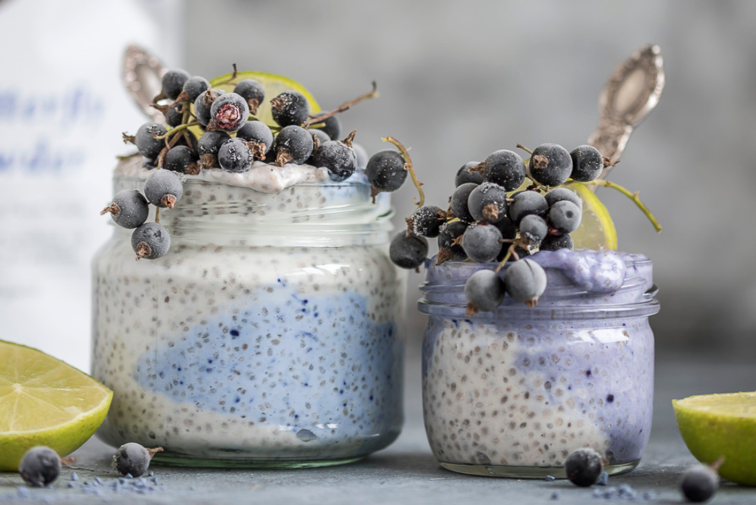 Two glass jars filled with chia pudding and blue butterfly pea powder, garnished with blueberries and a slice of lime